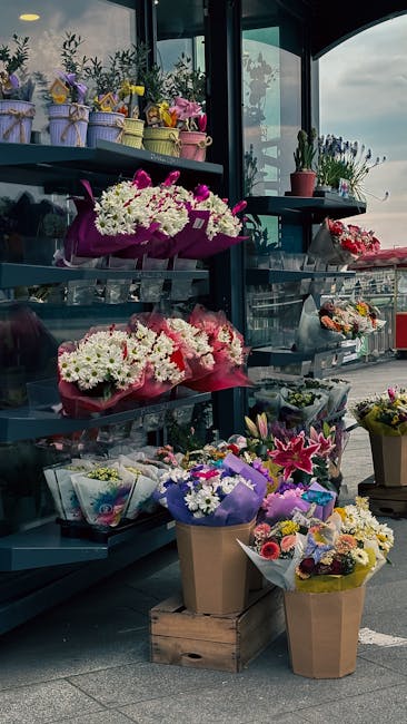 A display of fresh floral arrangements and bouquets at a flower shop, featuring a variety of flowers including white chrysanthemums, pink lilies, purple irises, and colorful mixed blooms. The flowers 
